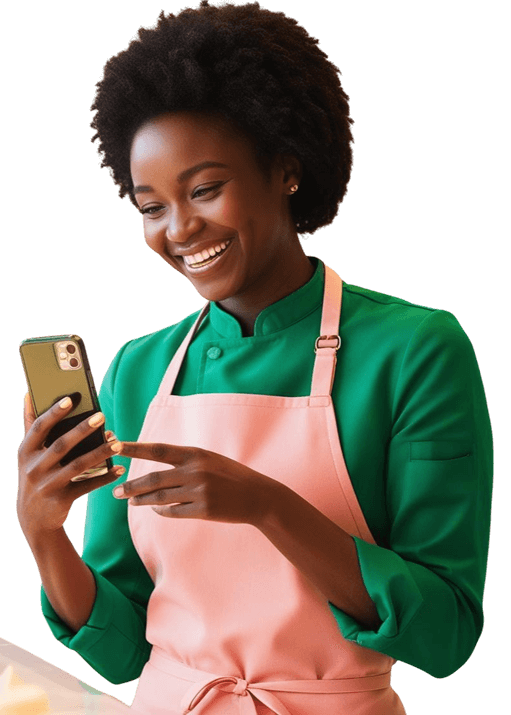 Confeiteira profissional sorrindo enquanto usa o aplicativo Confeitaria Agenda em seu celular, na cozinha da confeitaria